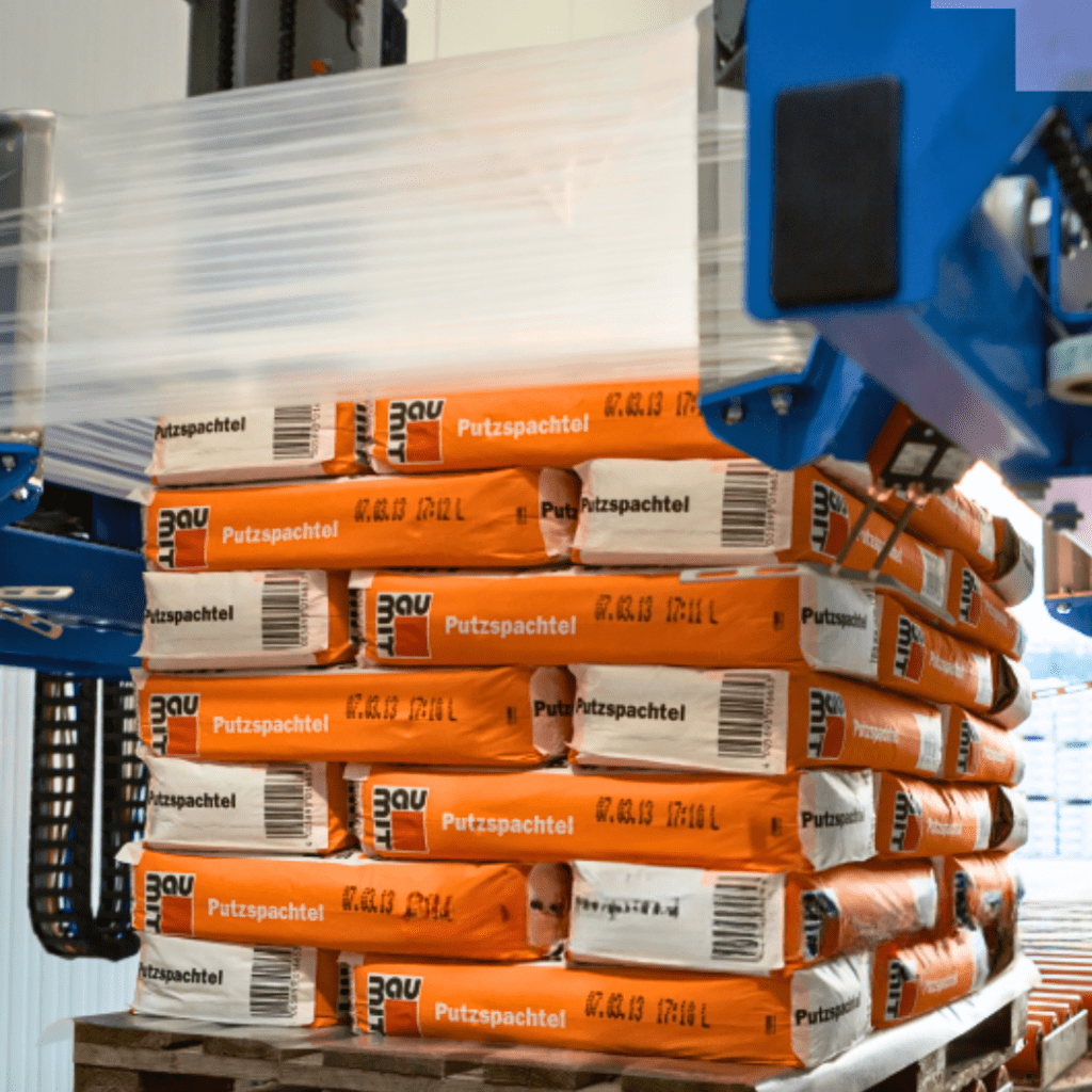 Stretch hood packaging equipment wrapping stacked products for flexible pallet protection.